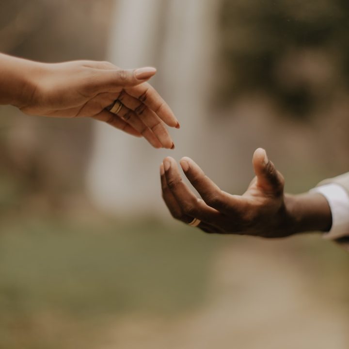 Sonstige Therapien Eine weiße und eine schwarze Hand, die sich annähern, als wollten sie sich berühren. Der Hintergrund ist unscharf.