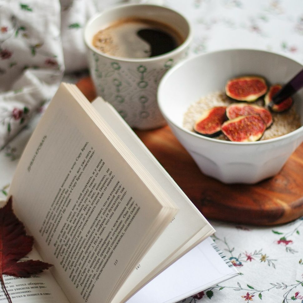 Frühstücks Porridge mit feigen, daneben ein Kaffee und ein aufgeschlagenes Buch