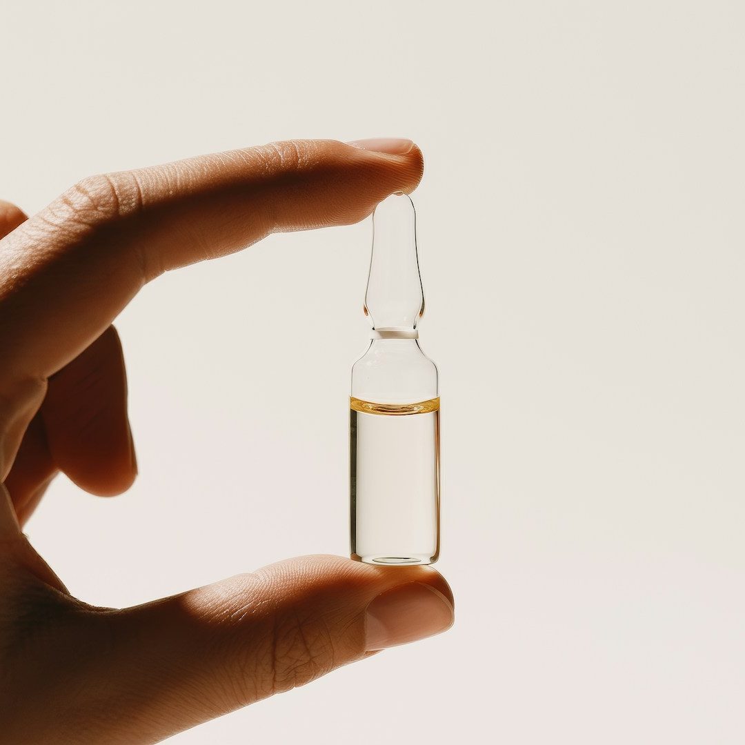 Sanum-Therapie Finger, die eine Ampulle zwischen Daumen und Zeigefinger halten, die Flüssigkeit ist ganz klar.