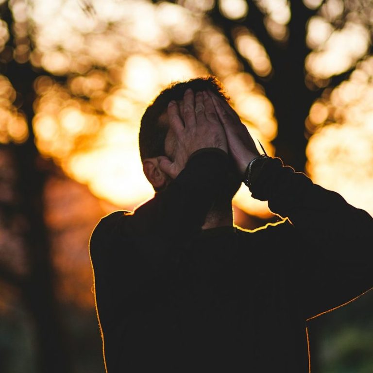 Schlafstörungen & Müdigkeit Mann, der im rötlichen Sonnenlicht, die Hände über die Augen legt