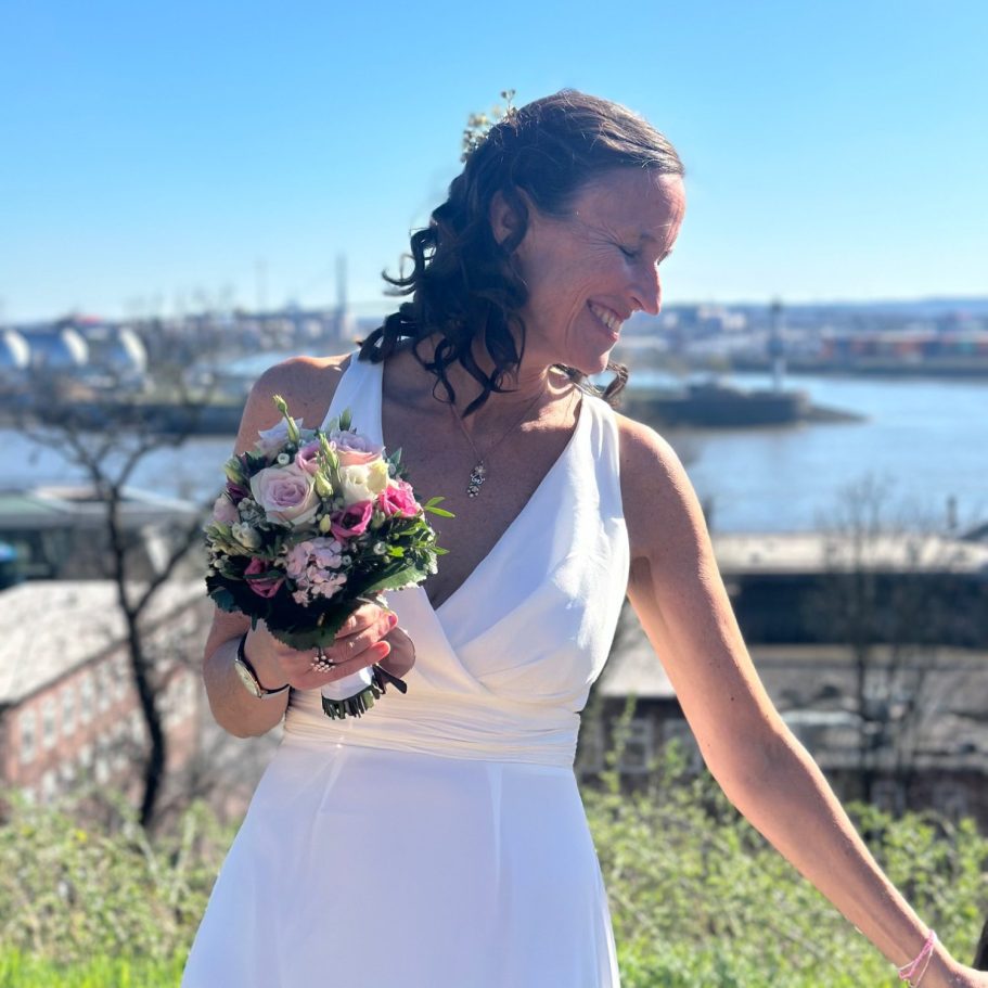 Hoch-Zeit Meike Völkner im Hochzeitskleid, hoch über der Elbe auf dem Altonaer Balkon. Sie schaut zur Seite und lächelt.