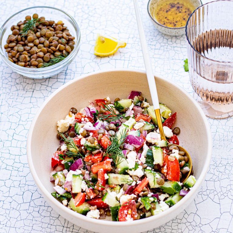 Gesunder Salat mit Schafskäse, Gurken, Tomaten, Kräutern, daneben Gewürz, Hülsenfrüchte und ein Glas Wasser